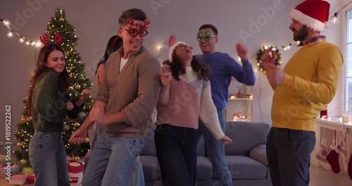 Christmas friends singing karaoke with microphone. A cheerful group of people shares happiness and dances at a home party near a festive tree. Captures joyful holiday friendship and cheer.