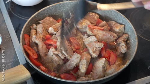 Cooking pork and tomatoes in a frying pan on the stove during the evening in the kitchen