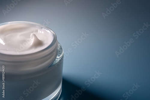 Skin care moisturizing cream in an open glass jar, showing a soft, whipped texture on a blue background