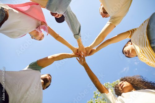 Group of friends stacking hands. Team of young diverse people standing in circle under clear blue summer sky and holding hands together. Bottom view. Friendship and teamwork concept