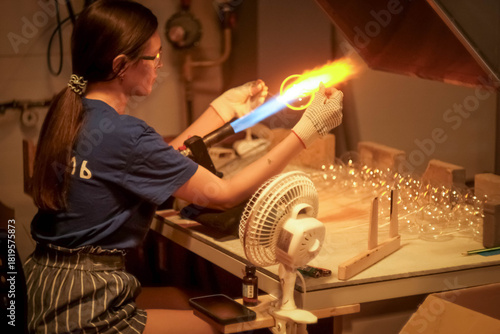 A young girl blows glass toys for the Christmas tree. Glass blower at a Christmas tree decorations factory. Fire and glass..