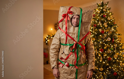 Man dressed as a poorly wrapped Christmas gift standing by a tree  