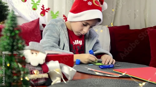 Cute boy preparing for Christmas cutting out paper decorations and garlands. Winter holidays. Christmas concept.
