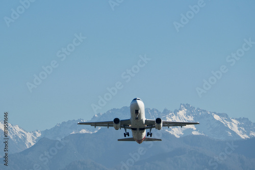 Airplane Climbing into Winter Sky Above Snowy Mountain Landscape. Powerful Takeoff of Commercial Airplane in Winter Mountain Setting