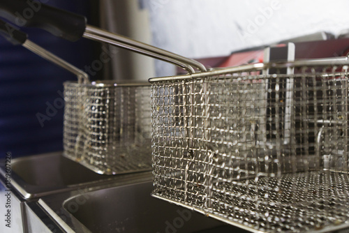 Close-up view of two professional deep fryers featuring stainless steel oil containers and metal frying baskets in a commercial kitchen setting. Clean industrial equipment designed for deep-frying.