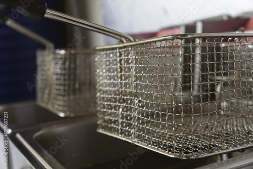 Close-up view of two professional deep fryers featuring stainless steel oil containers and metal frying baskets in a commercial kitchen setting. Clean industrial equipment designed for deep-frying.