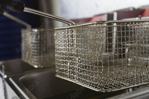 Close-up view of two professional deep fryers featuring stainless steel oil containers and metal frying baskets in a commercial kitchen setting. Clean industrial equipment designed for deep-frying.