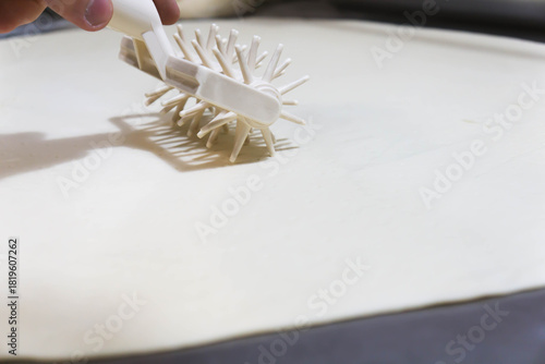 Close-up of a professional dough docker perforating pizza dough to prevent air bubbles during baking. Stainless-steel kitchen tool used in pizzerias and commercial kitchens. Close up. 