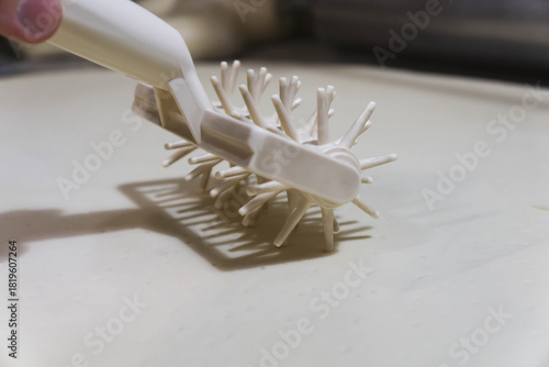 Close-up of a professional dough docker perforating pizza dough to prevent air bubbles during baking. Stainless-steel kitchen tool used in pizzerias and commercial kitchens. Close up. 