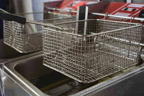 Close-up view of two professional deep fryers featuring stainless steel oil containers and metal frying baskets in a commercial kitchen setting. Clean industrial equipment designed for deep-frying.