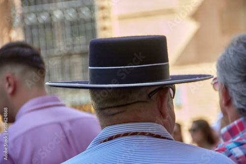 A man in traditional Andalusian attire with a wide brim hat stands among the crowd during the Cruces de mayo andaluzas en Granada festive moment. street scene