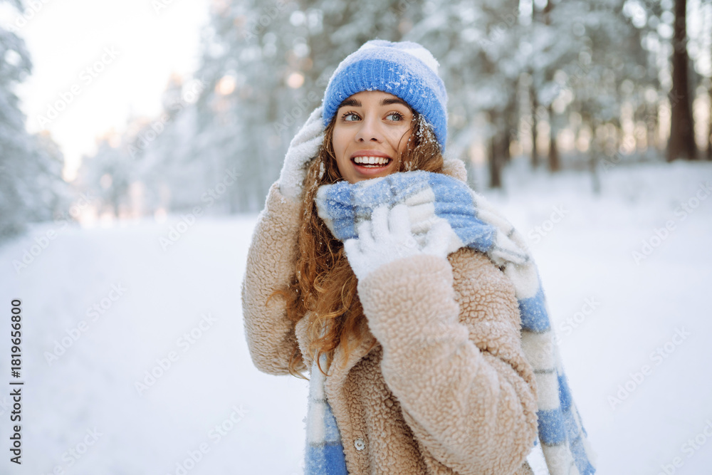 Obraz premium A curly-haired woman in warm clothing is having fun in a snowy forest at sunset. A young woman enjoys a sunny day outdoors. Nature concept, walk. Winter day.