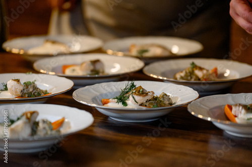 Numerous plates with portions of fish and side dishes on a wooden banquet table.