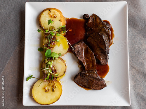 Gourmet sliced roasted or braised beef with sauce and potatoes served on white plate.