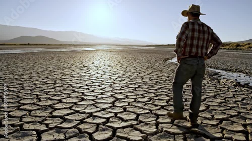 Cowboy in hat standing in arid dry desert landscape under bright sunlight