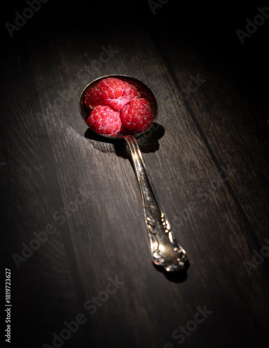 Framboises dans une cuillère sur planche bois, intérieur sombre,  verticale