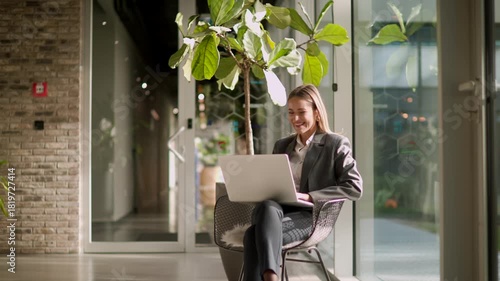 In a cozy, sunlit space, a woman works on her laptop, enjoying the greenery around her while being productive and relaxed.
