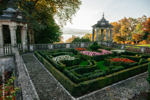 Stone gazebos and manicured hedge maye with lake and mountains in autumn. Scenic autumn maze garden with colorful foliage, lake and mountain view