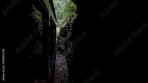 View of the Flåmsbana Railway train in Norway from one of its windows, traveling through an area of ​​lush mountain nature and just entering a tunnel