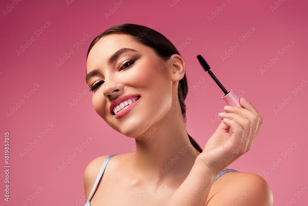 Fototapeta premium Beautiful Young Woman Modeling with Mascara on Pink Background Highlighting Makeup and Style