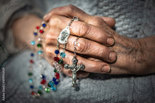 Elderly hands clasped together, adorned with colorful rosary beads, symbolizing faith and family, representing the passage of time and the bond between generations