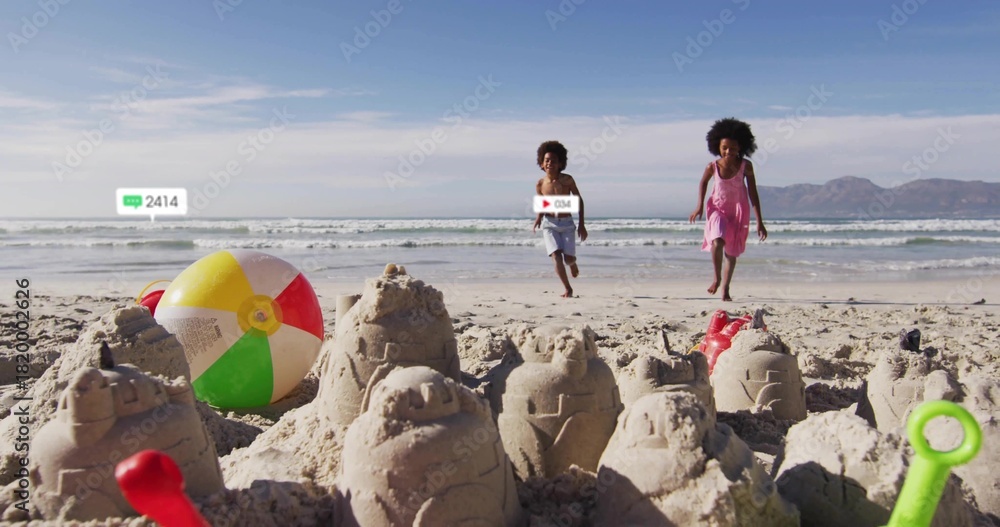 Naklejka premium Running kids in pink sundress and swim trunks racing on beach toward sandcastles with colorful ball
