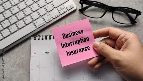Business Interruption Insurance: Hand Holding Sticky Note with Text over Calendar and Keyboard for Corporate Risk Management