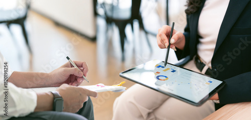 Close-up of two business professionals in formal attire working together, reviewing data on a digital tablet and signing a document.