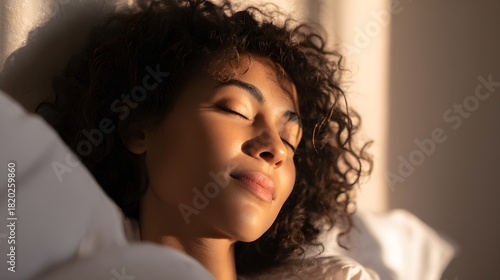 Young woman with dark curly hair peacefully sleeping as warm sunlight illuminates her face