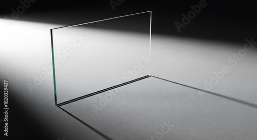 A stark minimalist composition featuring a transparent glass panel illuminated by a dramatic shaft of light against a dark background