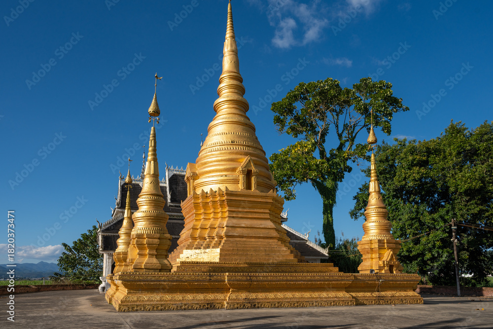 Fototapeta premium Bright Golden Buddhist Stupa and Pagoda Against a Clear Blue Sky
