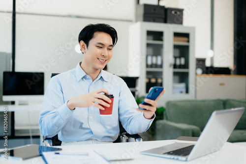 Wallpaper Mural Confident  Asian businessman typing laptop computer and digital tablet while holding coffee at office Torontodigital.ca
