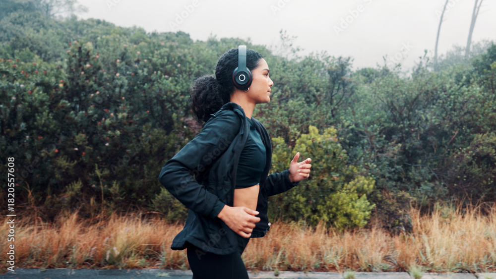 Fototapeta premium Fitness, woman and running with headphones in road for exercise, music playlist and cardio podcast. Athlete, person and workout in nature with audio streaming, pace training and endurance challenge