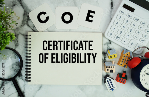 COE Certificate of Eligibility text written on notepad with house model, calculator, magnifying glass and alarm clock on marble background