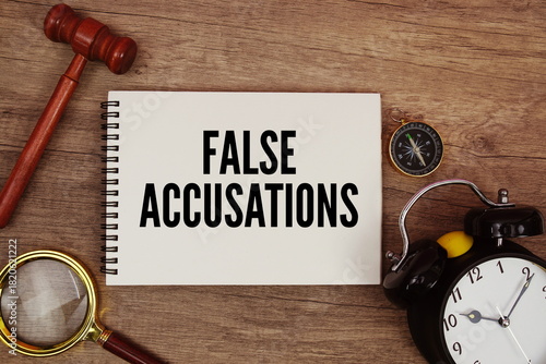 False Accusations message written on notepad with alarm clock, wood gavel and magnifying glass flat lay on wooden background
