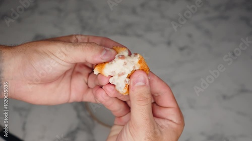 Male hands breaking a fried crispy hot croquette revealing the creamy filling inside