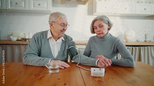 Senior people controlling blood pressure at home, using tonometer, portrait. Aged married couple caring about health after 60, stay healthy and active in old age, happy and healthy grandparents