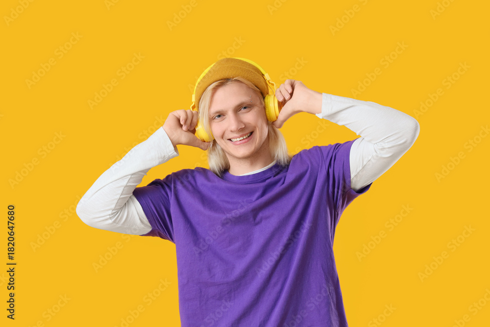 Fototapeta premium Young blonde man in hat with headphones on yellow background