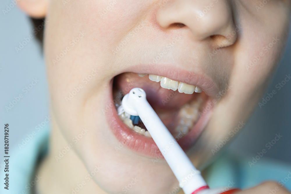 Naklejka premium Young child brushes teeth with electric toothbrush in bright bathroom during morning routine