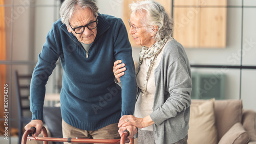 An elderly couple helps each other while using a walking frame