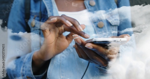 Tapping woman wearing denim jacket and white top at window, phone and earphone cable showing, nails