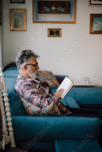 Older man reading a book on a cozy blue couch