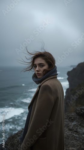 Pensive woman with hair blowing in wind by dramatic coastline and rough sea