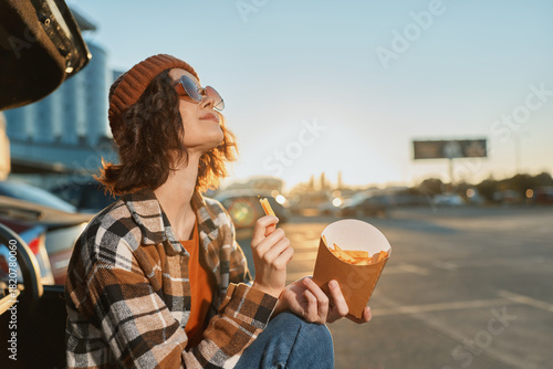 woman fries car sunset beanie sunglasses parking casual enjoying golden hour glow with authenticity and candid lifestyle vibe, mindful living and emotional storytelling in urban roadside scene