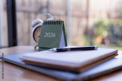 2026 desk calendar with notebook, pen, and clock on wooden table in cozy daylight workspace, perfect for planning productivity, and time management content.
