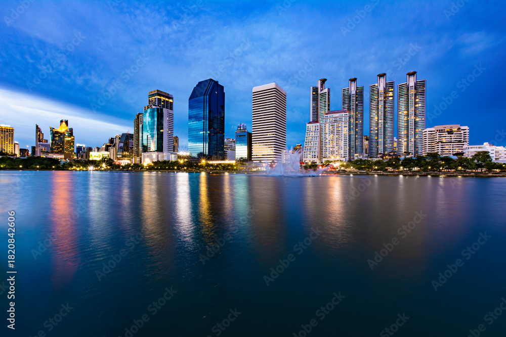 Fototapeta premium Beautiful view of Bangkok's lake at dusk (blue hour) in Benchakitti Park. Bangkok cityscape at sunset at Benjakitti Park.
