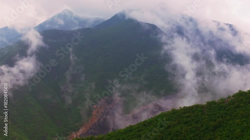 Cinematic aerial view of misty green mountain peaks covered in low fog. Moody cloud forest landscape.