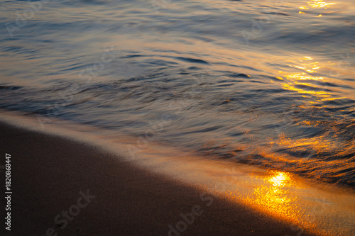 Sea wave washing sandy coastline with smooth long exposure motion, tranquil water texture and minimalistic seascape mood at sunset.