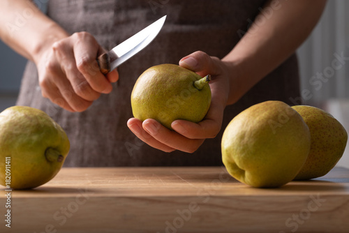 Hand holding kitchen knife and cutting pear on wooden board