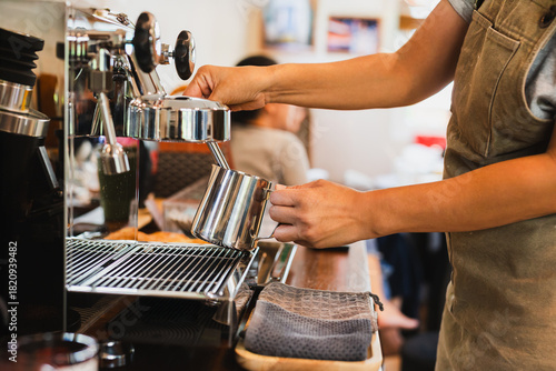 Photography Woman barista steaming jug of milk at coffee machine in a cafe.